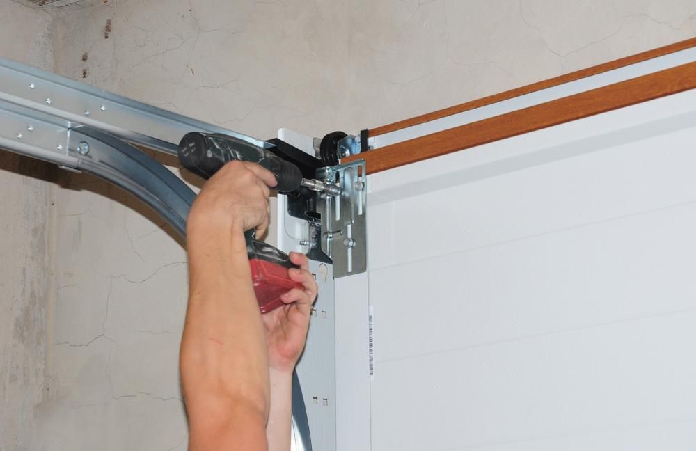 A Person Is Fixing A Garage Door With A Screwdriver — Mick’s Garage Doors In Alice River, QLD