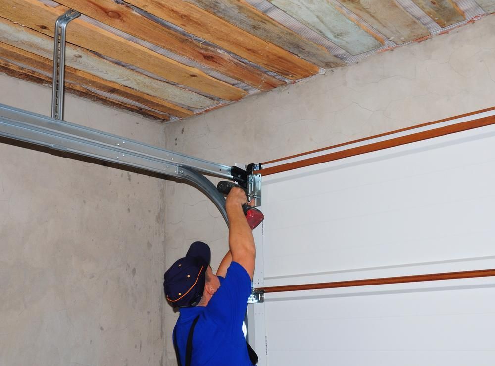 A Man Is Fixing A Garage Door With A Drill — Mick’s Garage Doors In Alice River, QLD