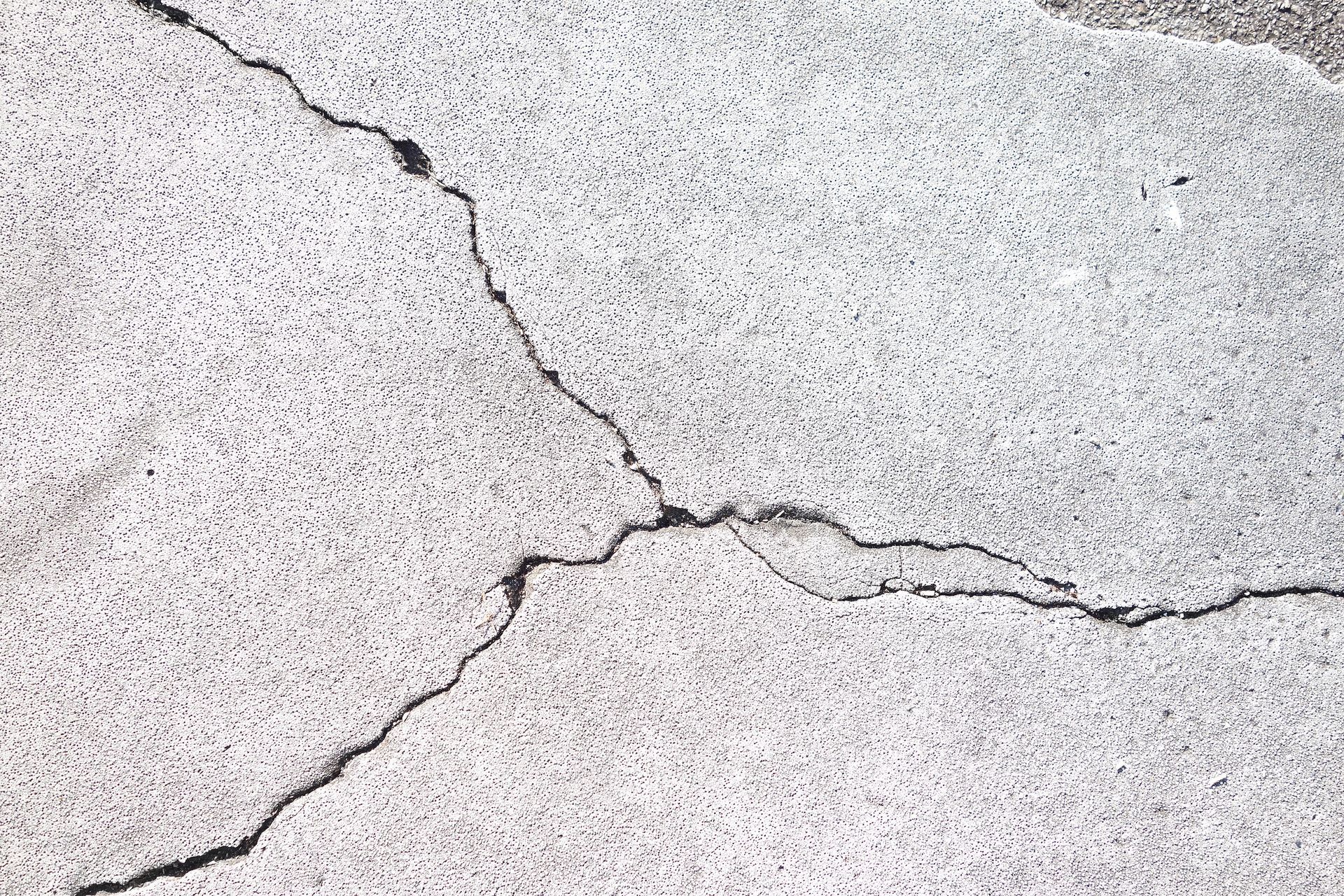 A vertical crack in a gray concrete house foundation below beige siding and a pile of dirt.