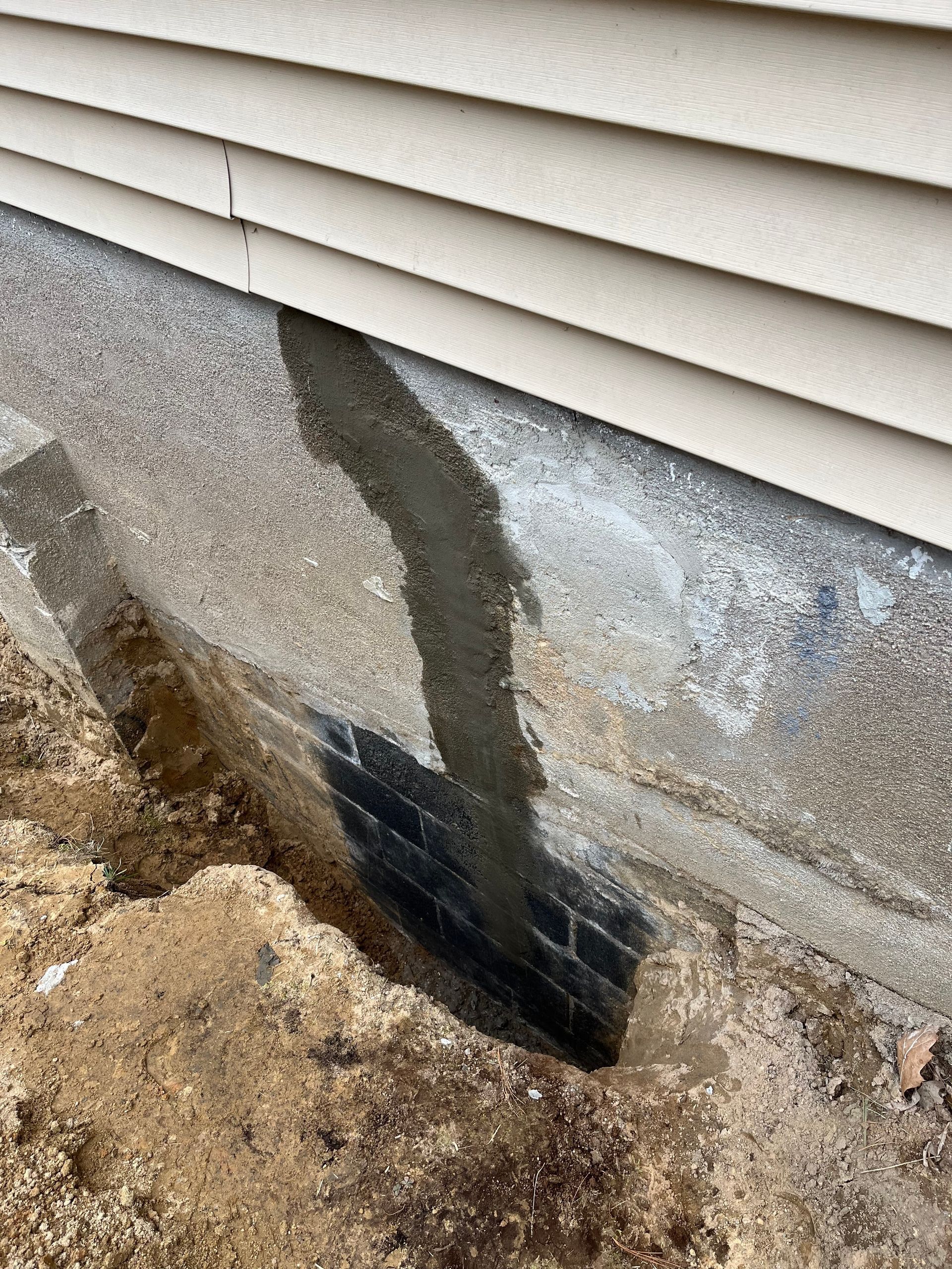 A concrete foundation wall with a fresh vertical patch of grey mortar over a crack, extending into the soil below.