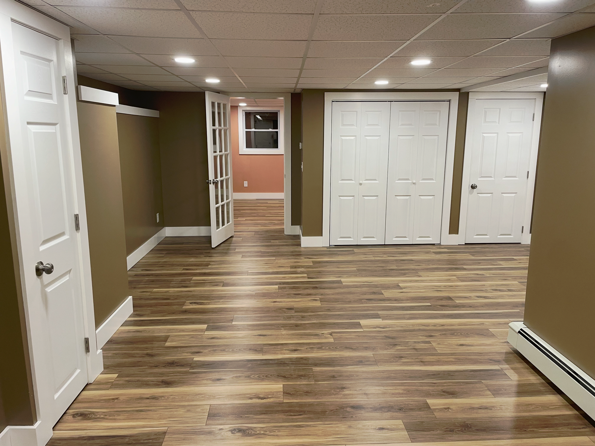 Basement room featuring brown walls, wood-look flooring, drop ceiling, multiple white doors, and a glass-paned door.