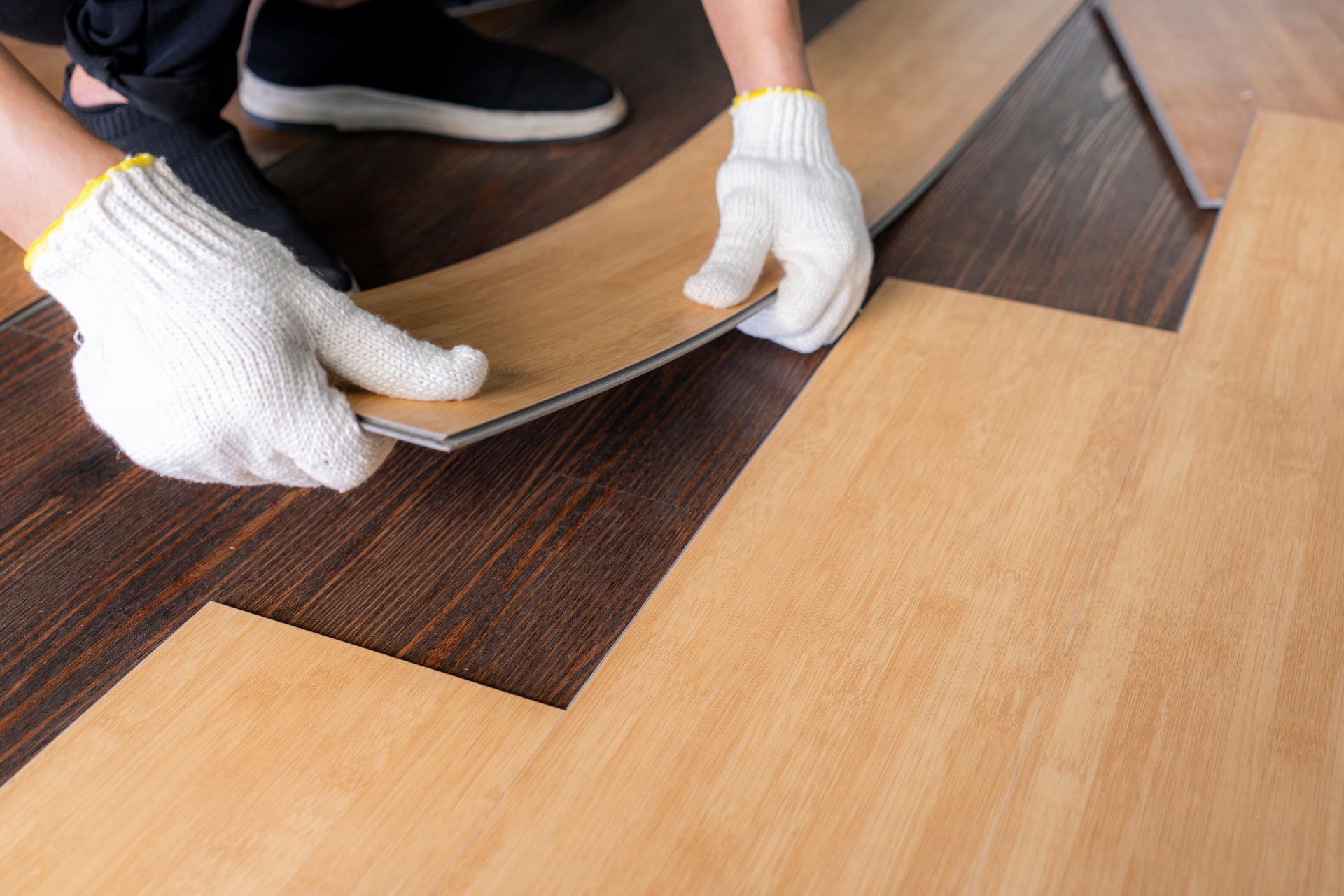 A person is laying a piece of vinyl flooring on a wooden floor
