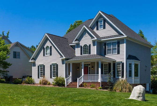 A large white house with a large porch is sitting on top of a lush green lawn.