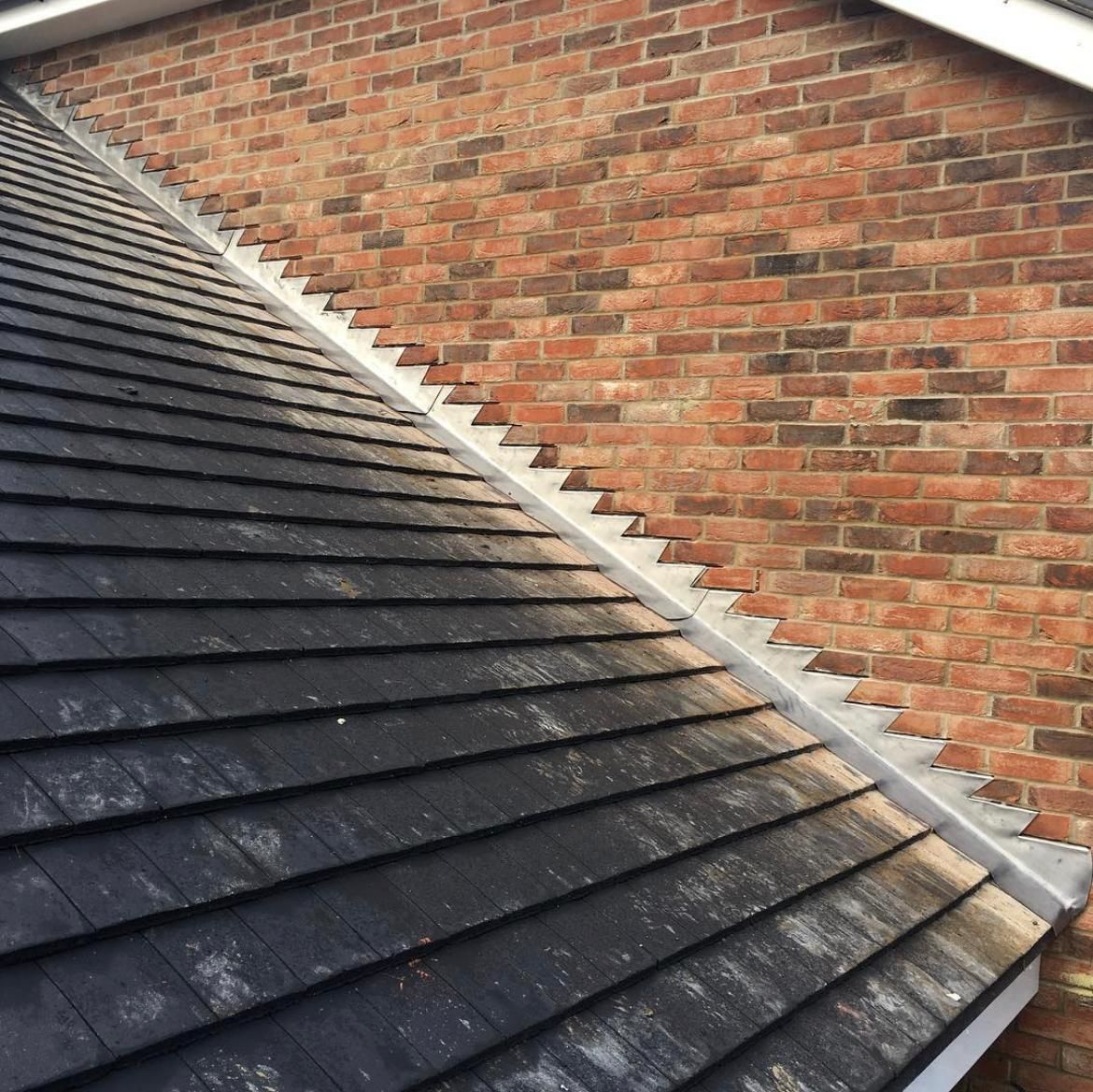 Dark roof tiles meet a brick wall at an angle. Flashing creates a metal strip where the roof and wall meet.