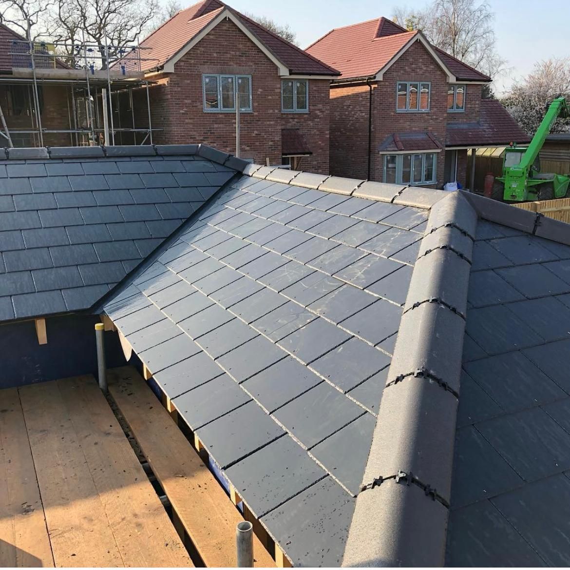 Gray tile roof under construction with finished brick houses in the background.