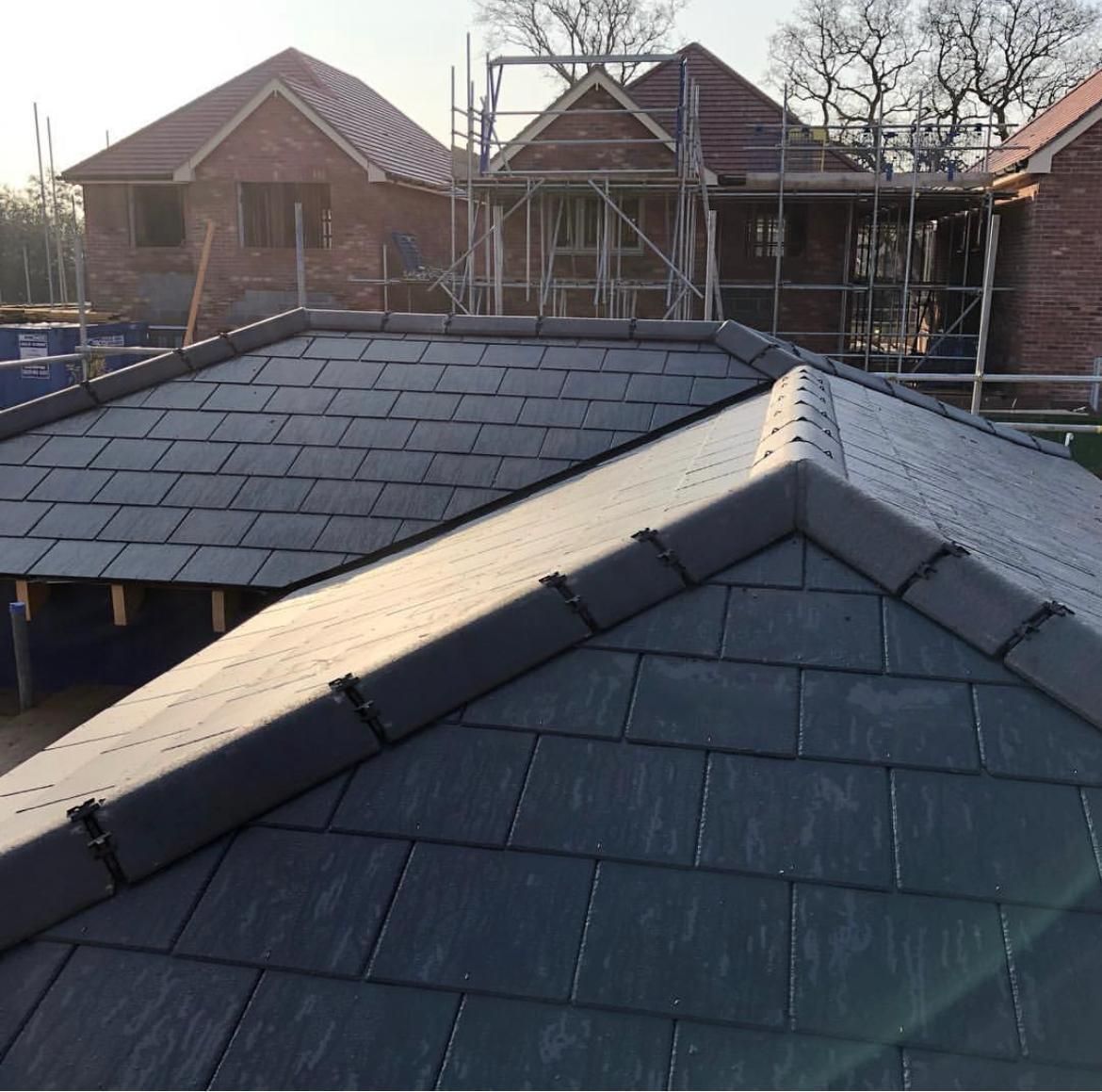 A close-up view of a dark gray tiled roof with other houses under construction in the background.