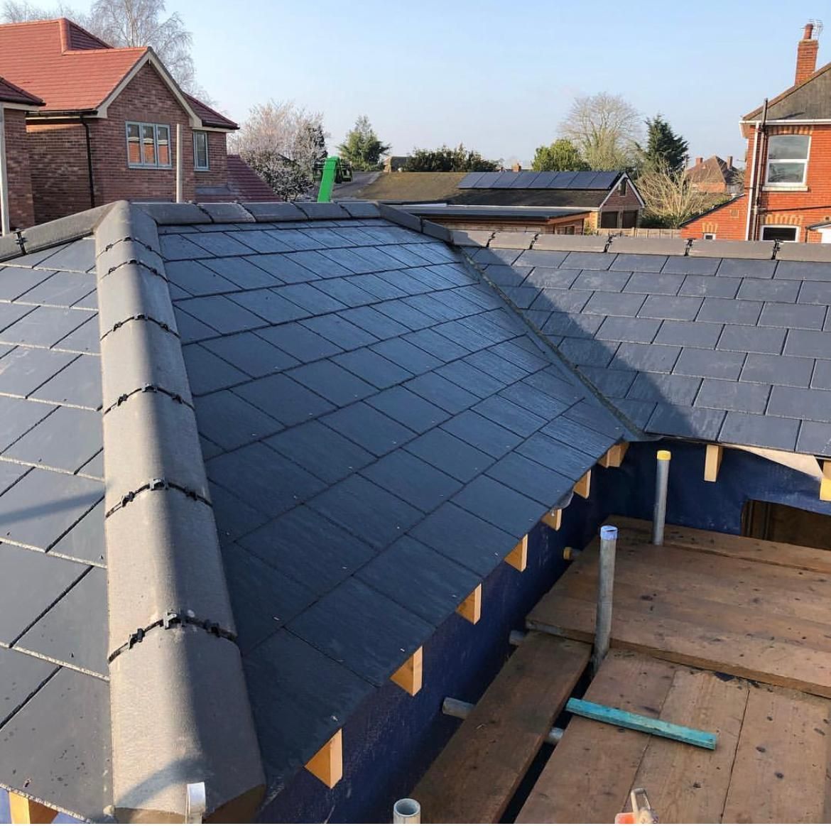 Partially completed dark gray tiled roof on a house, with surrounding houses and scaffolding visible.
