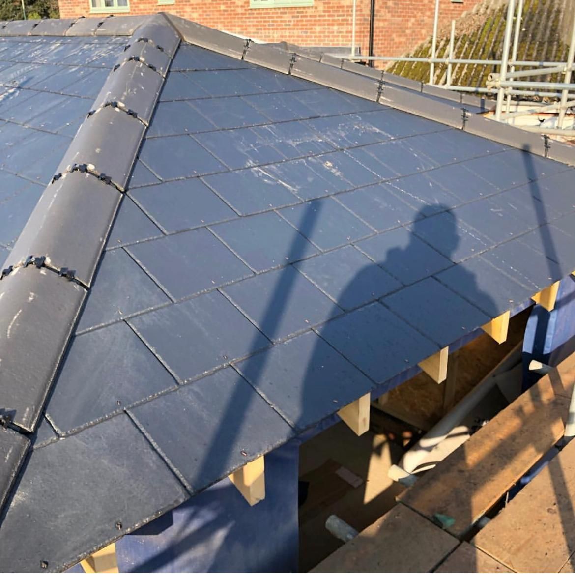 Newly tiled roof with dark gray slates. Construction site visible, showing scaffolding and building materials.