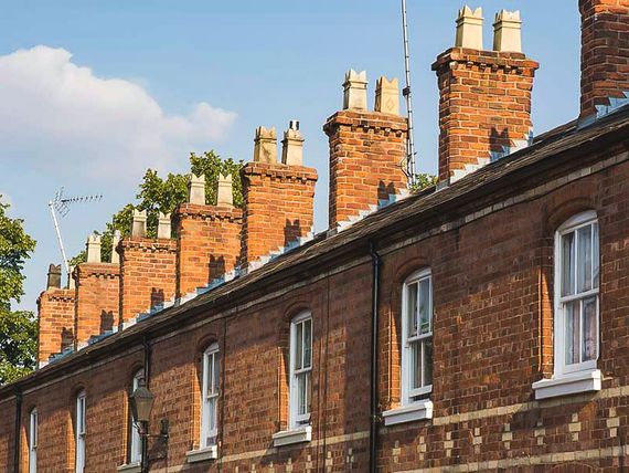 Row of brick houses with white-framed windows and ornate chimneys against a blue sky.