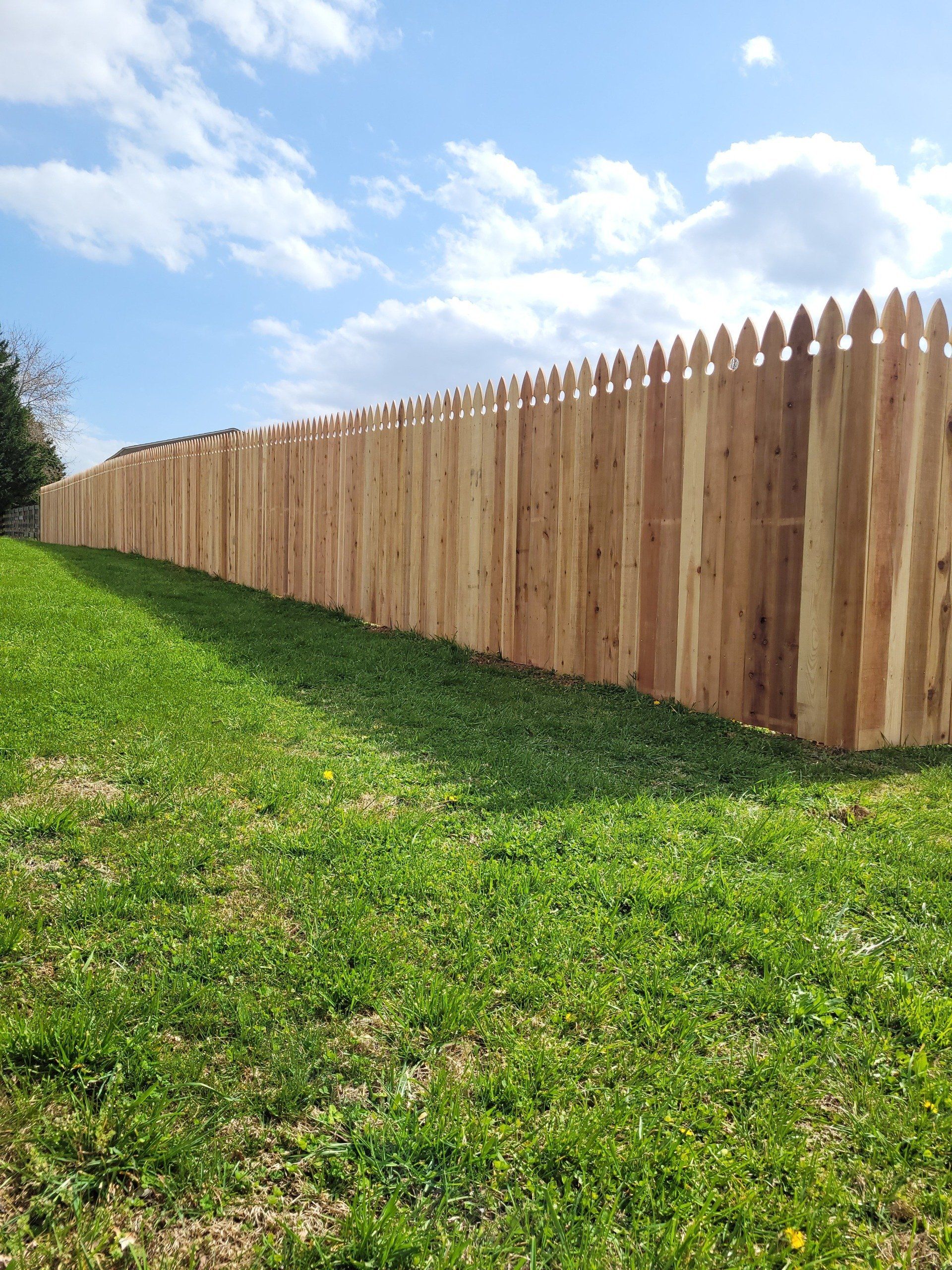 Wooden picket fence on a grassy hill under a blue sky with scattered clouds.