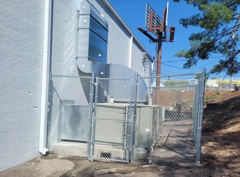 Exterior of a building with a fenced enclosure. Air vent and sign visible. Sunny day.