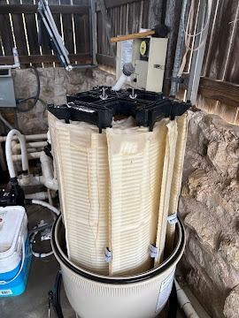 Dirty pool filter cartridge in a utility area, with black housing and beige pleated filter inside a bucket-like base