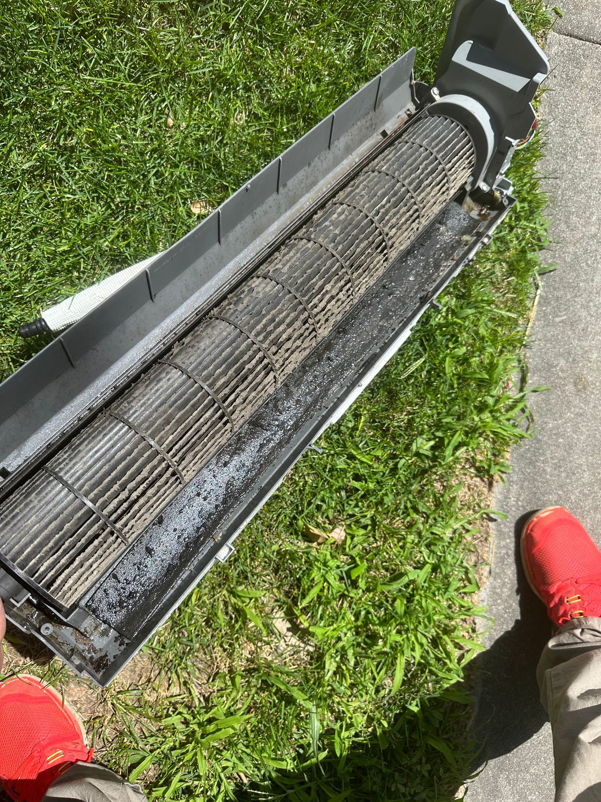 A person is standing next to a dirty air conditioner.