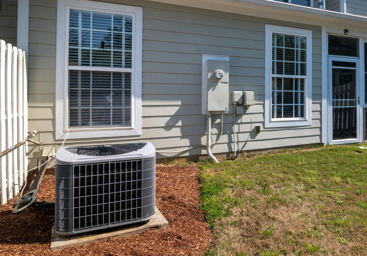 An air conditioner is sitting outside of a house next to a window.