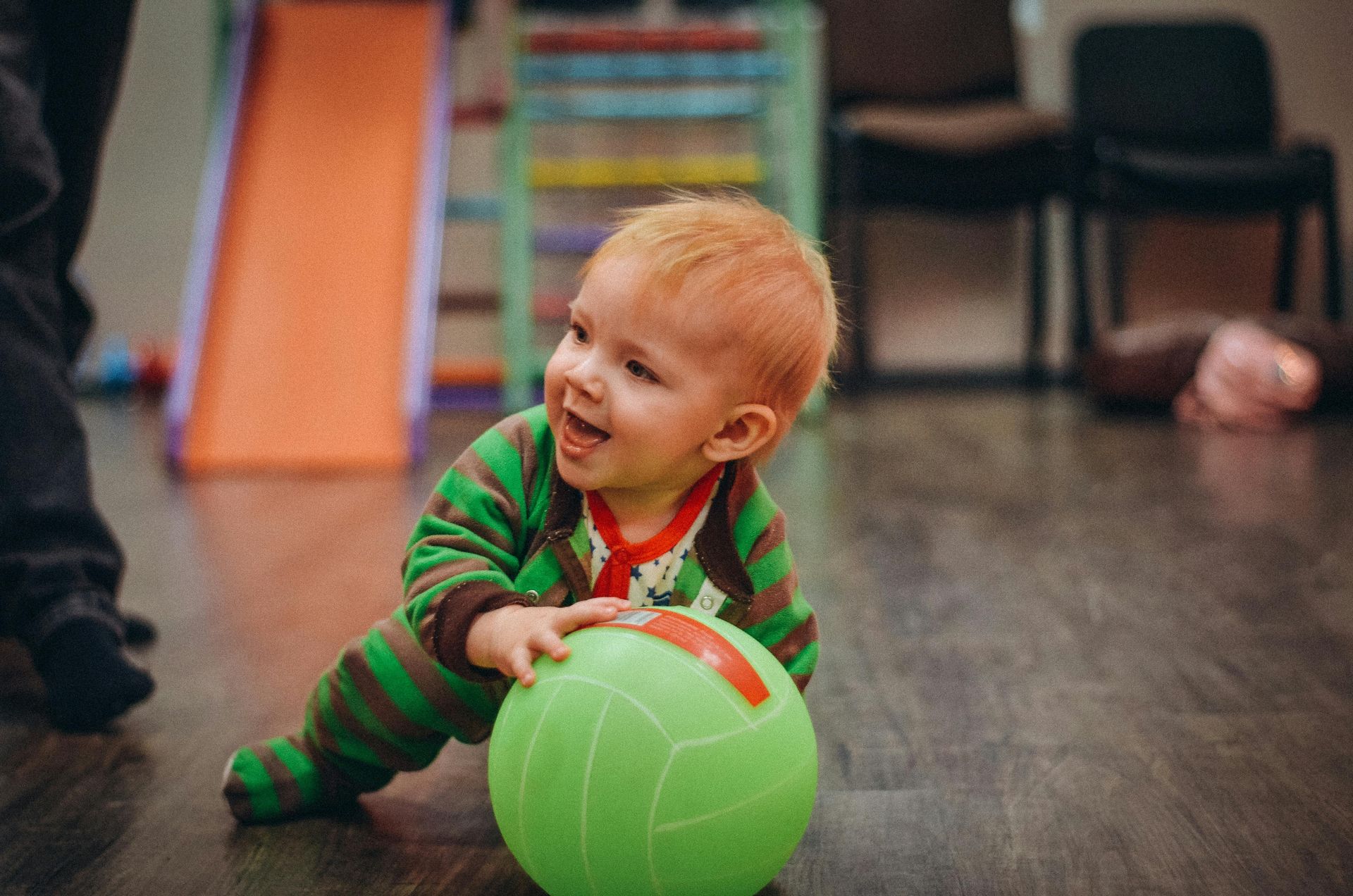 Toddler in green striped pajamas playing with a bright green ball indoors, smiling on the floor