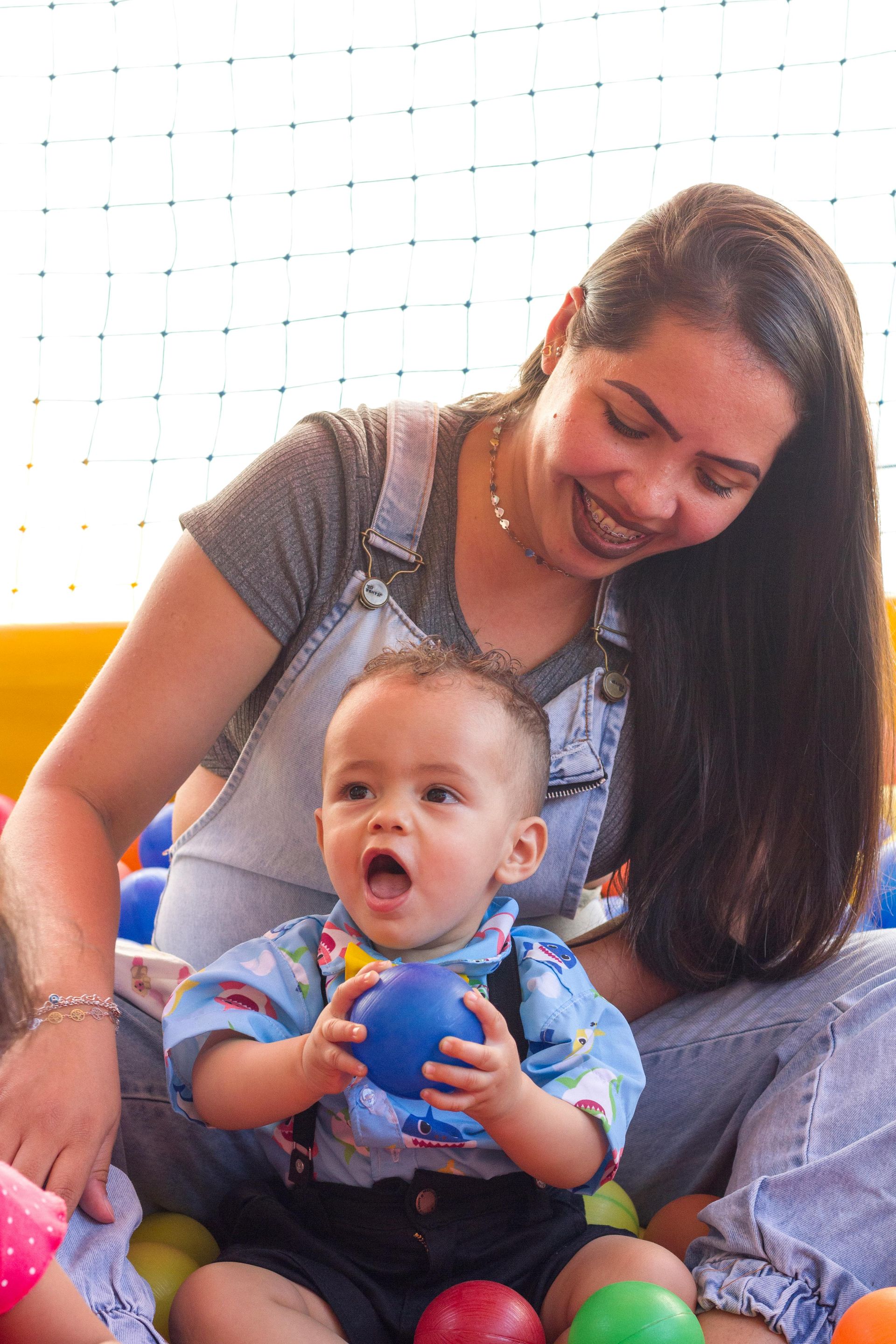 Woman smiling at a baby holding a blue cup on the floor, with a bright window behind them
