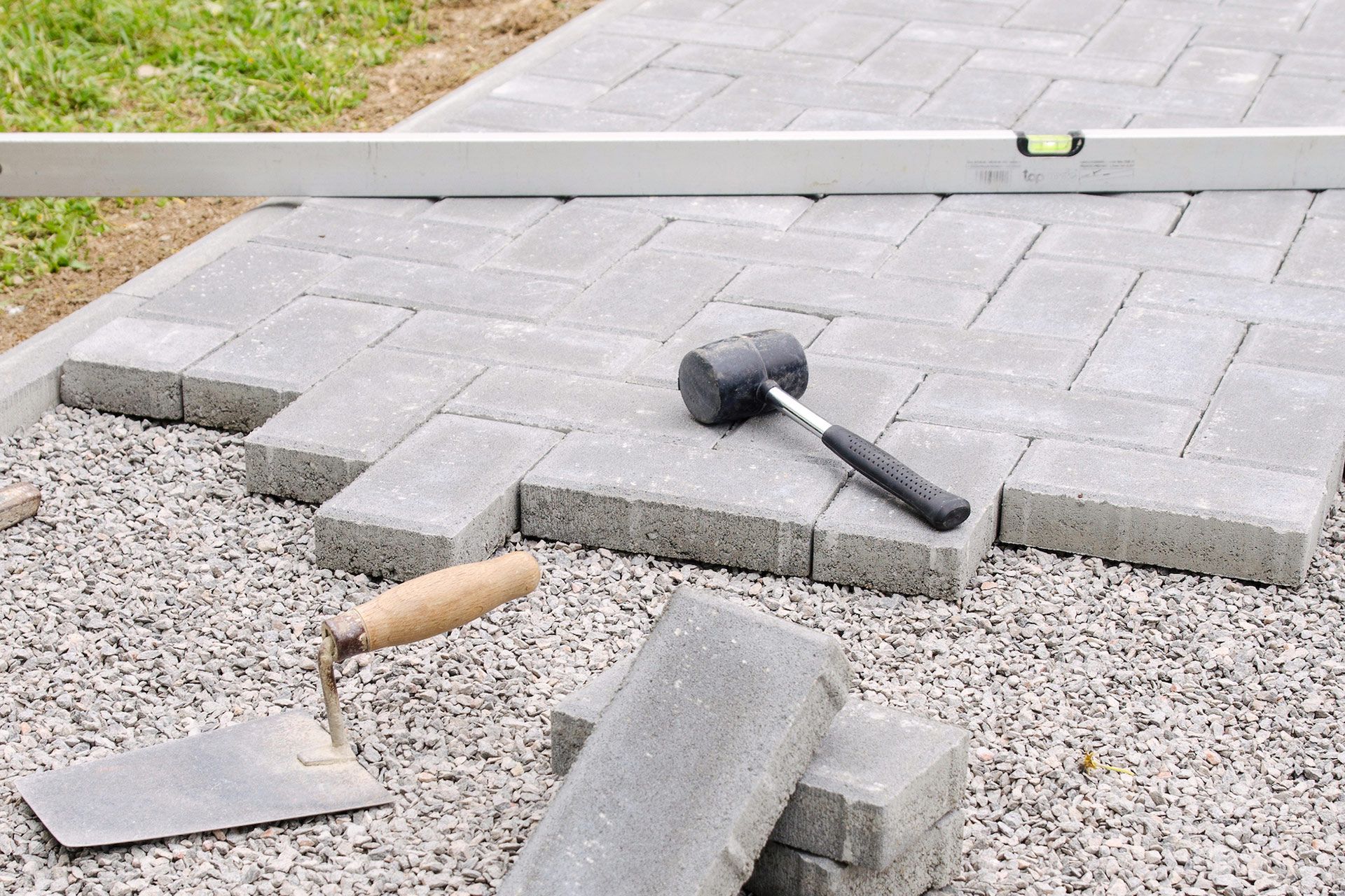 Installing brick pavers on gravel base with level, mallet, and trowel.
