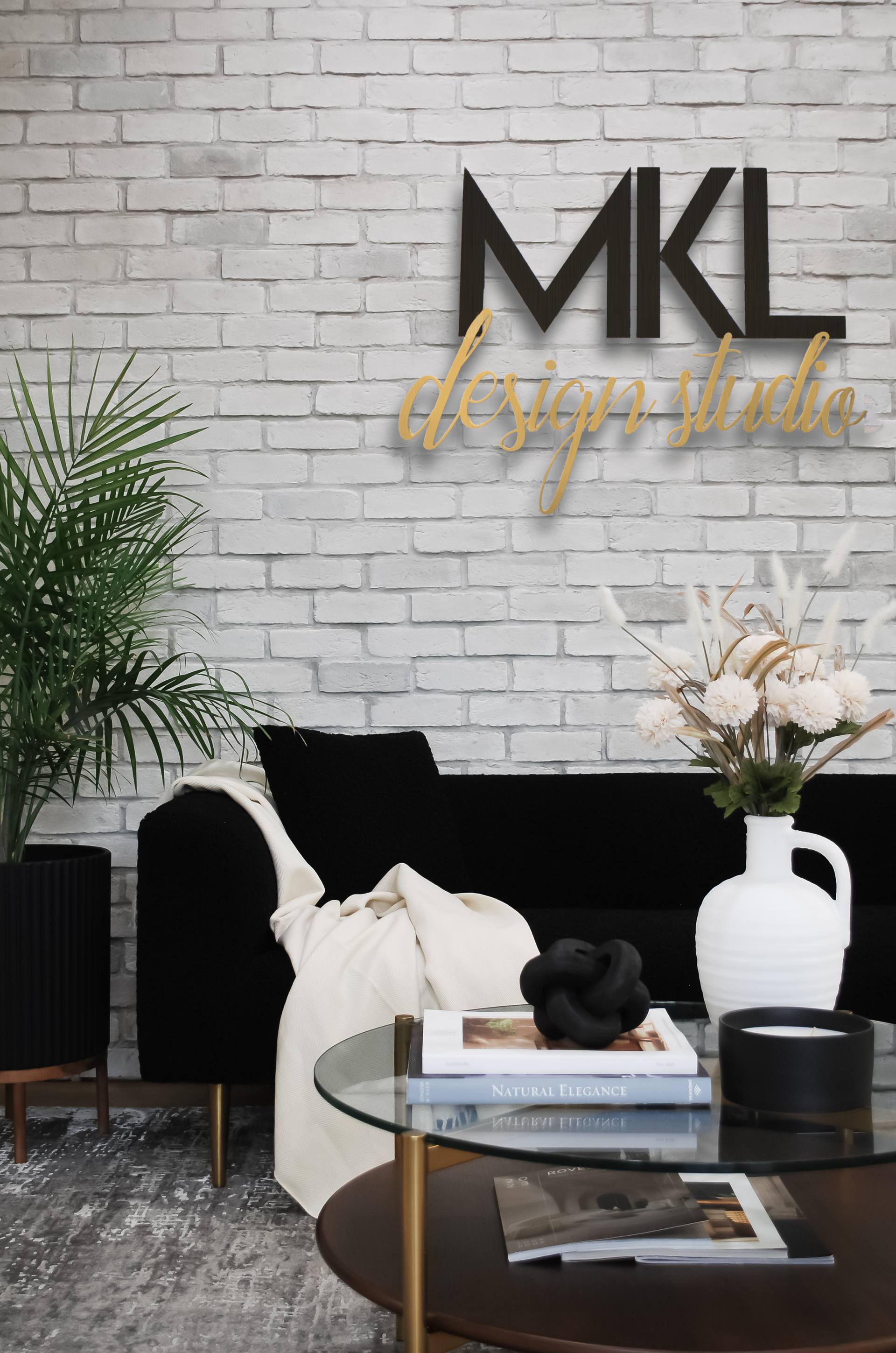 A modern living room with a black couch, coffee table, and brick wall with a design studio logo.