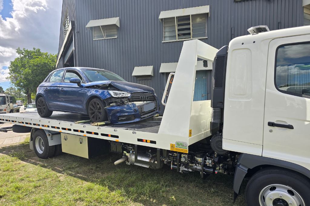 A blue car is sitting on top of a tow truck.