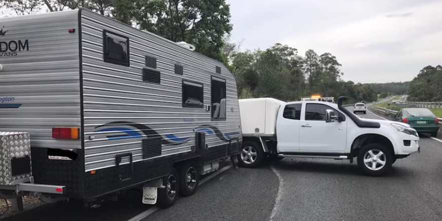 A white truck is towing a trailer down a road.