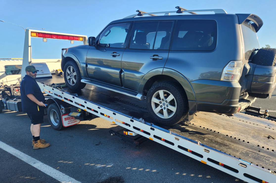 A man is standing next to a tow truck with a car on it.