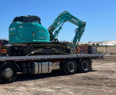 A kobelco excavator is on the back of a flatbed truck