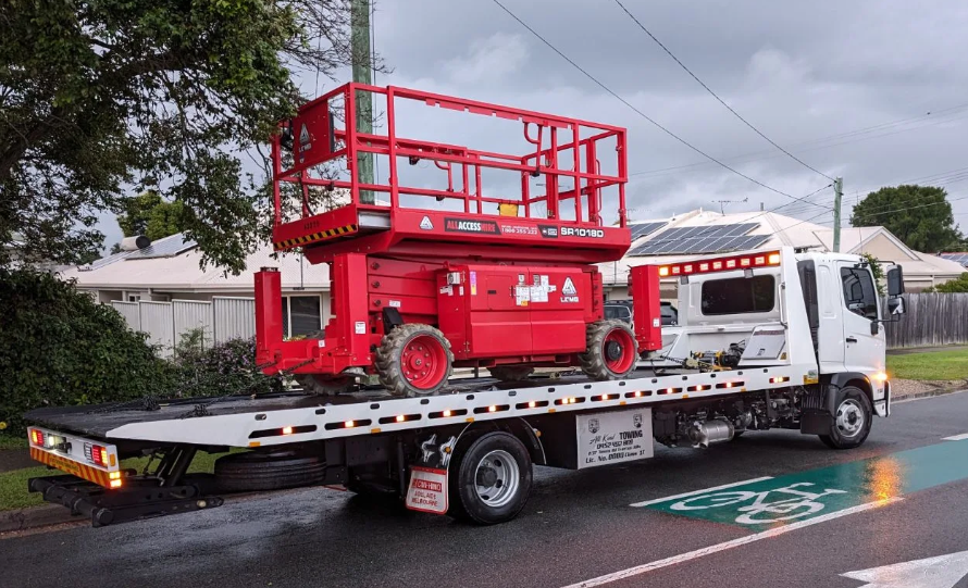 A red scissor lift is on the back of a tow truck.