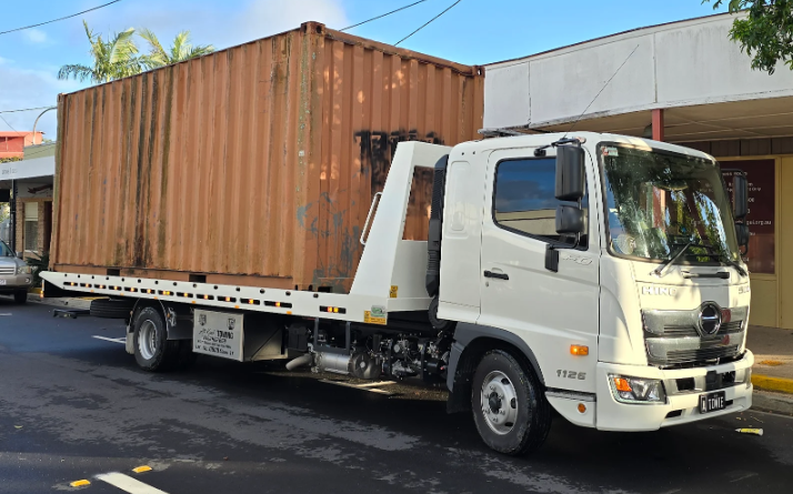 A tow truck with a container on the back is parked in front of a building.
