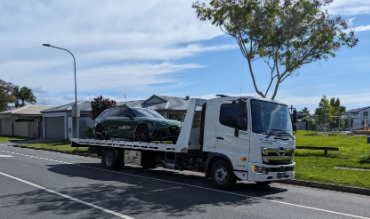 A tow truck with a car on the back is parked on the side of the road.