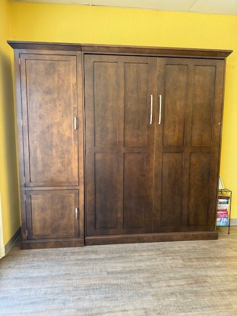Dark wooden wardrobe against a yellow wall in a mostly empty room