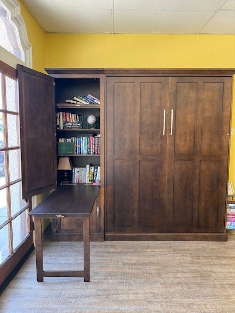 Wooden desk and storage cabinet against a yellow wall, with an open side shelf and window light on the left.