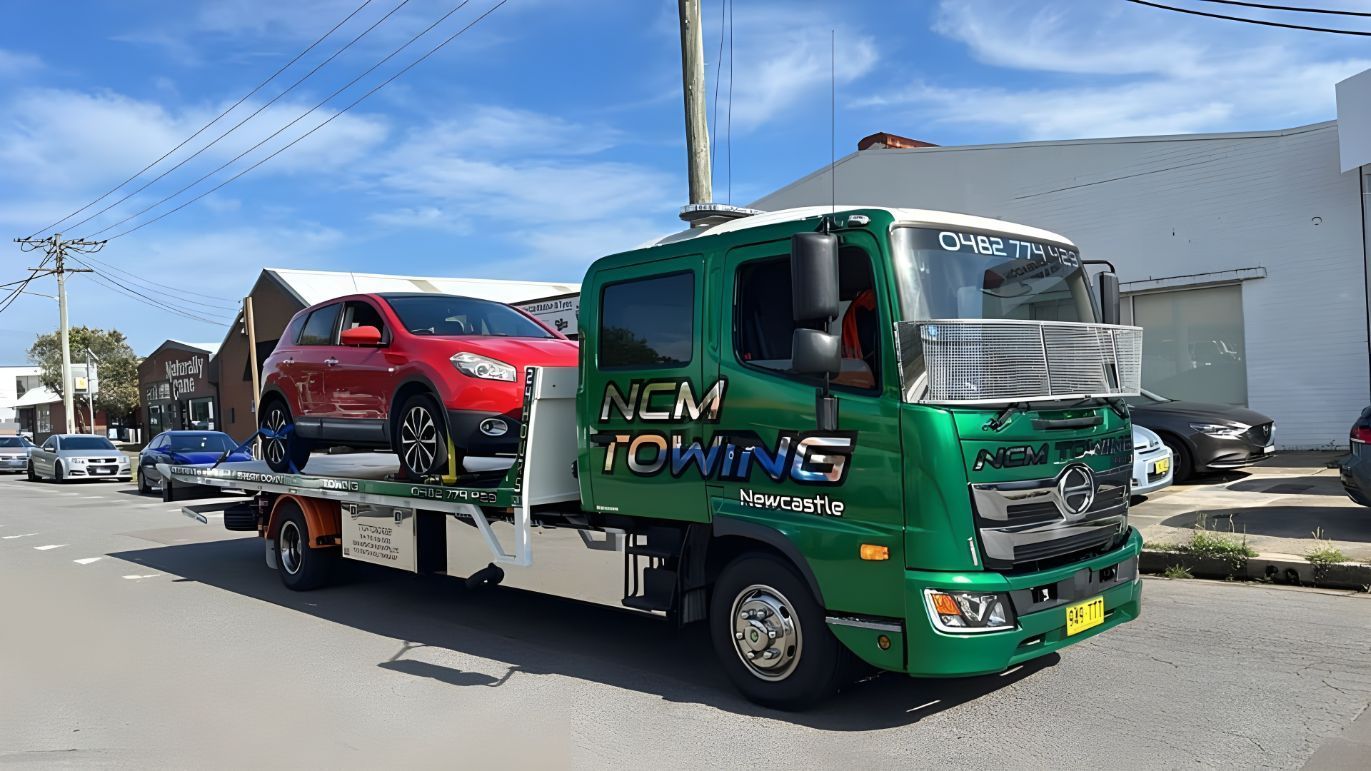 Green Tow Truck With a Red Car on the Back is Parked on the Side of the Road — NCM Towing Newcastle In Stockton, NSW
