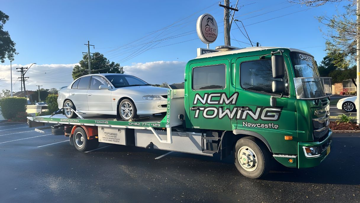 Green Towing Truck is Towing a White Car — NCM Towing Newcastle In Medowie, NSW