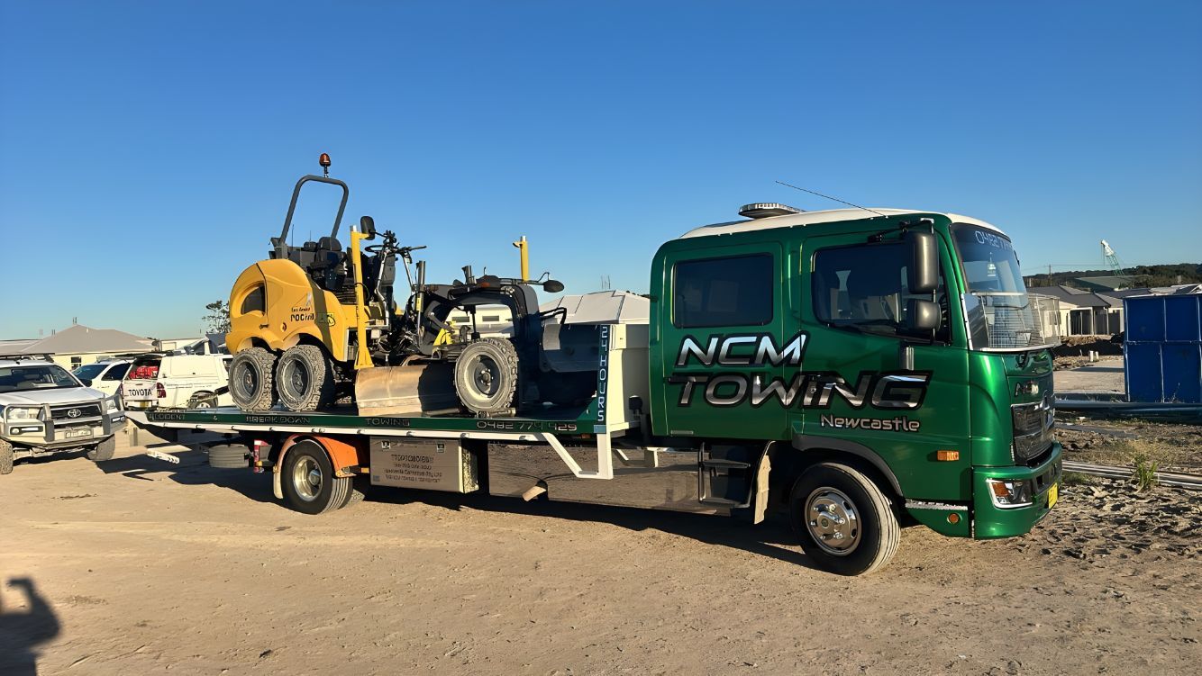 Green Tow Truck is Carrying a Bulldozer on the Back of It — NCM Towing Newcastle In Broadmeadow, NSW
