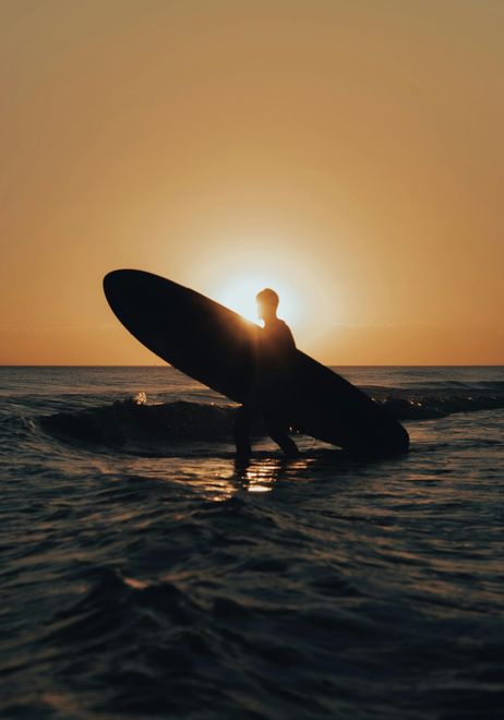 Person Carrying A Surfboard At Sunset In Shallow Ocean — Coastal Vibez In Ourimbah, NSW