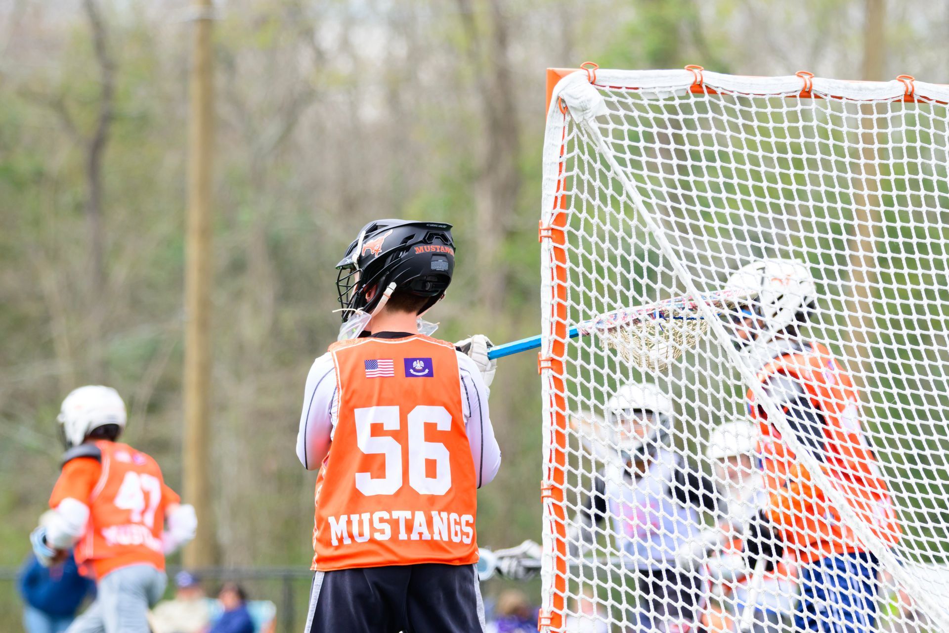 Lacrosse player in orange jersey #56 stands near the goal during an outdoor game.