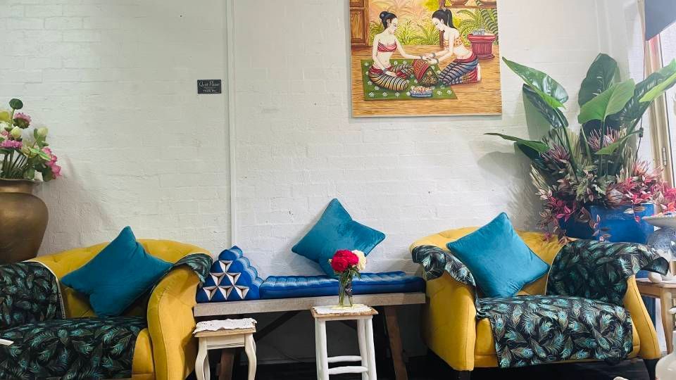 Cozy living room with patterned chairs, yellow cushions, blue pillows, side tables, and a wall painting.