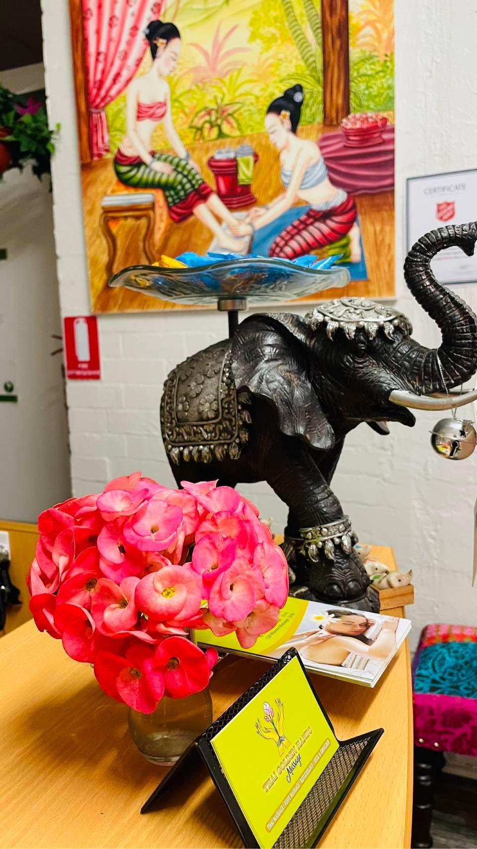 Black elephant figurine beside bright pink flowers on a table, with colorful wall art in the background