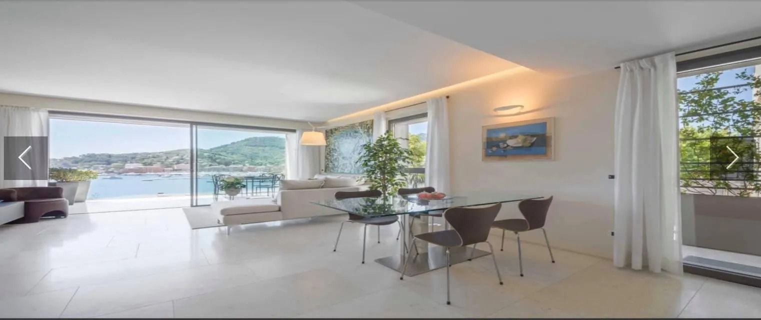 Luminoso e moderno soggiorno-sala da pranzo con vista sull'oceano attraverso ampie finestre e tavolo da pranzo in vetro.
