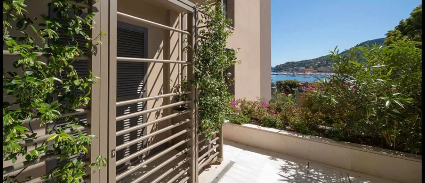 Balcone soleggiato con pergolato, piante e vista sul mare e sulle colline.