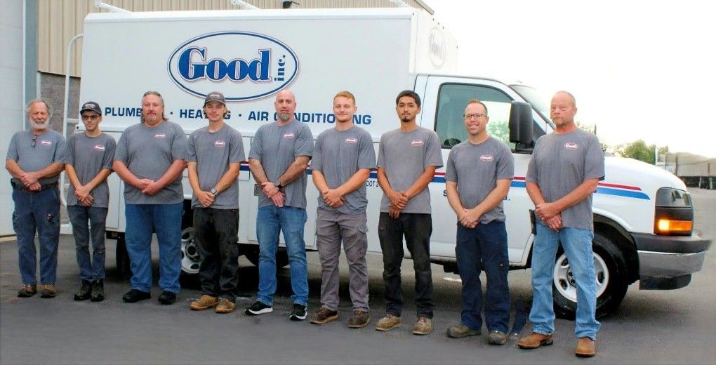 Nine people in gray shirts stand in front of a white truck with