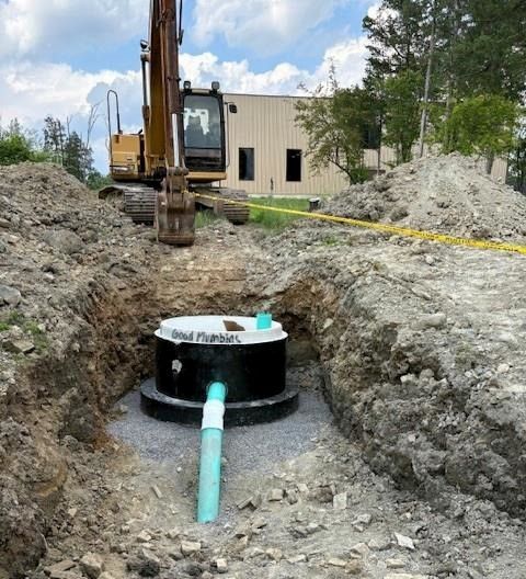 An excavator is lowering a septic tank into a trench at a construction site.