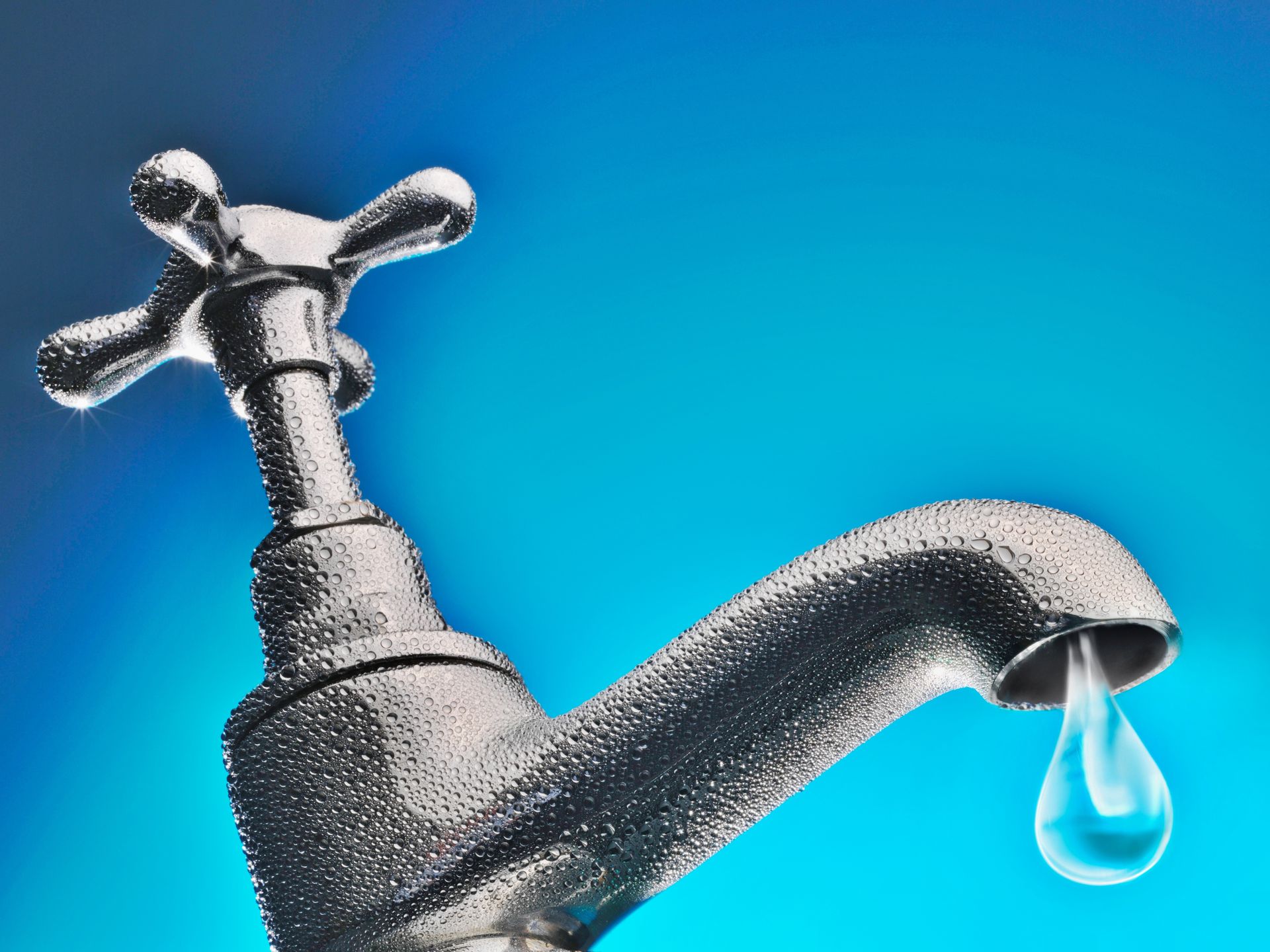 Chrome faucet with water droplet, blue background.