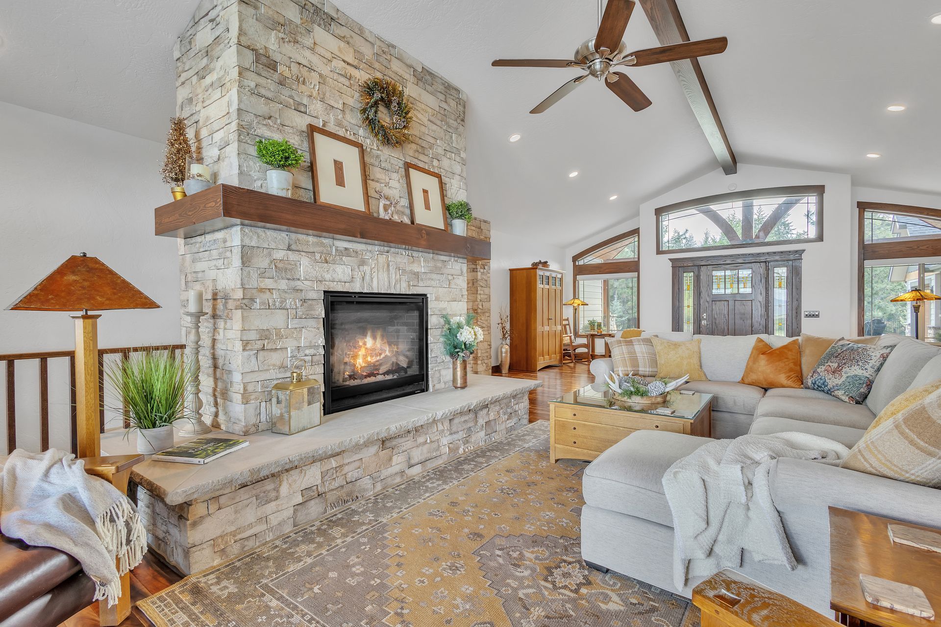 Cozy living room with stone fireplace, light-colored sectional sofa, and wooden ceiling fan.