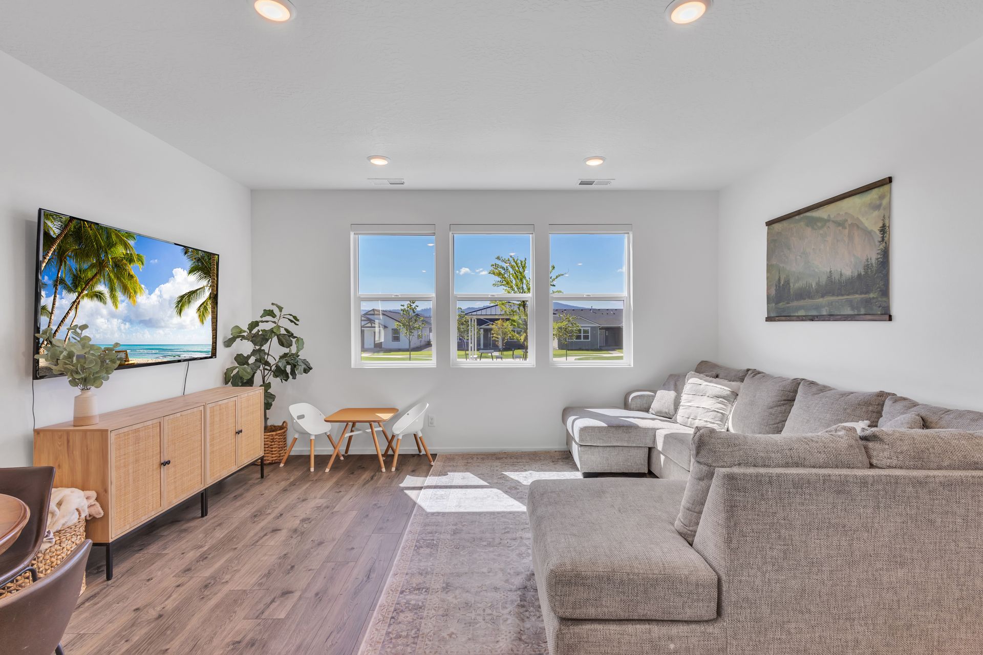 Living room with a grey sectional sofa, TV, wood console, and windows overlooking the outside.