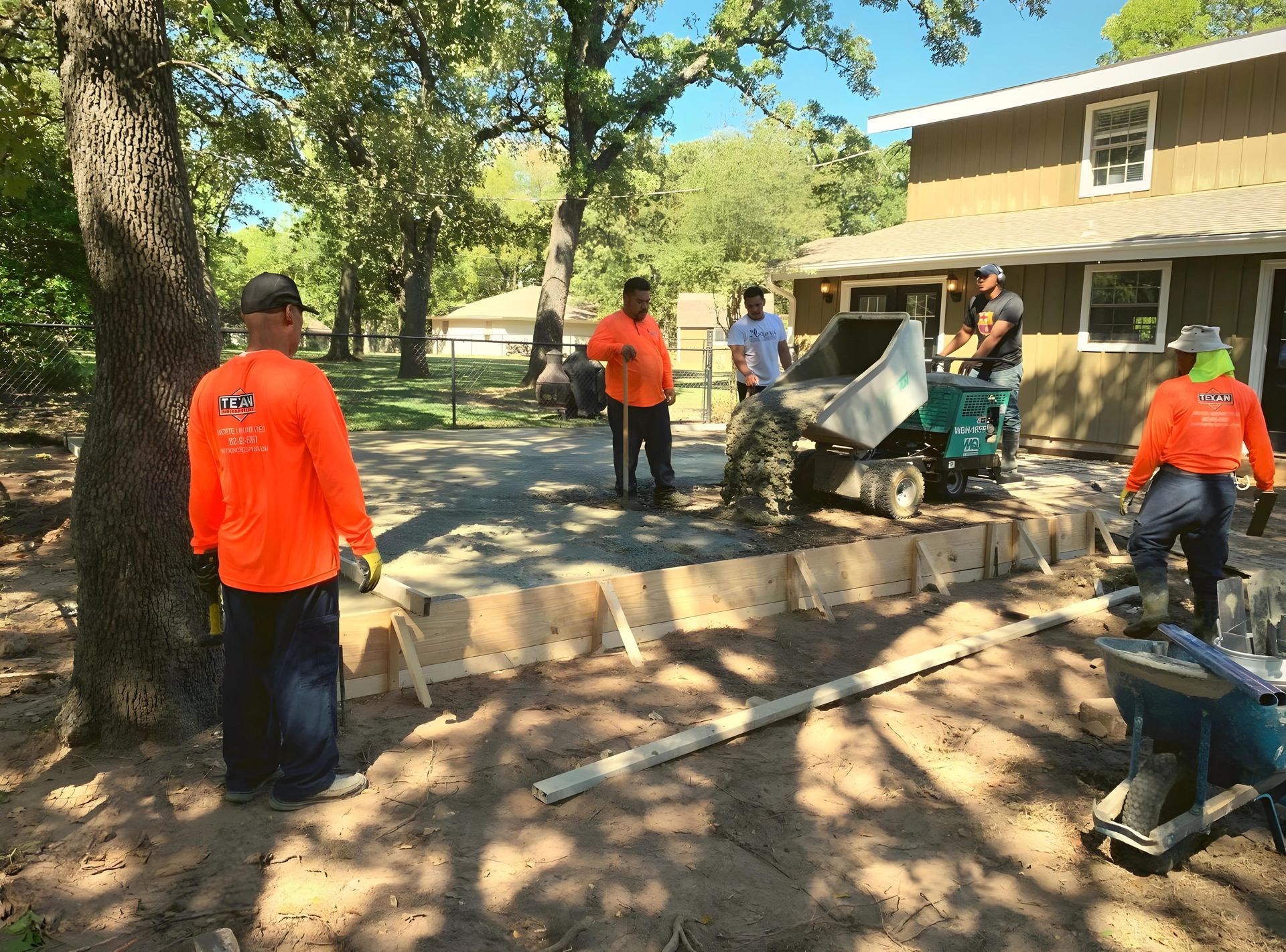 A group of construction workers are working on a driveway in front of a house.