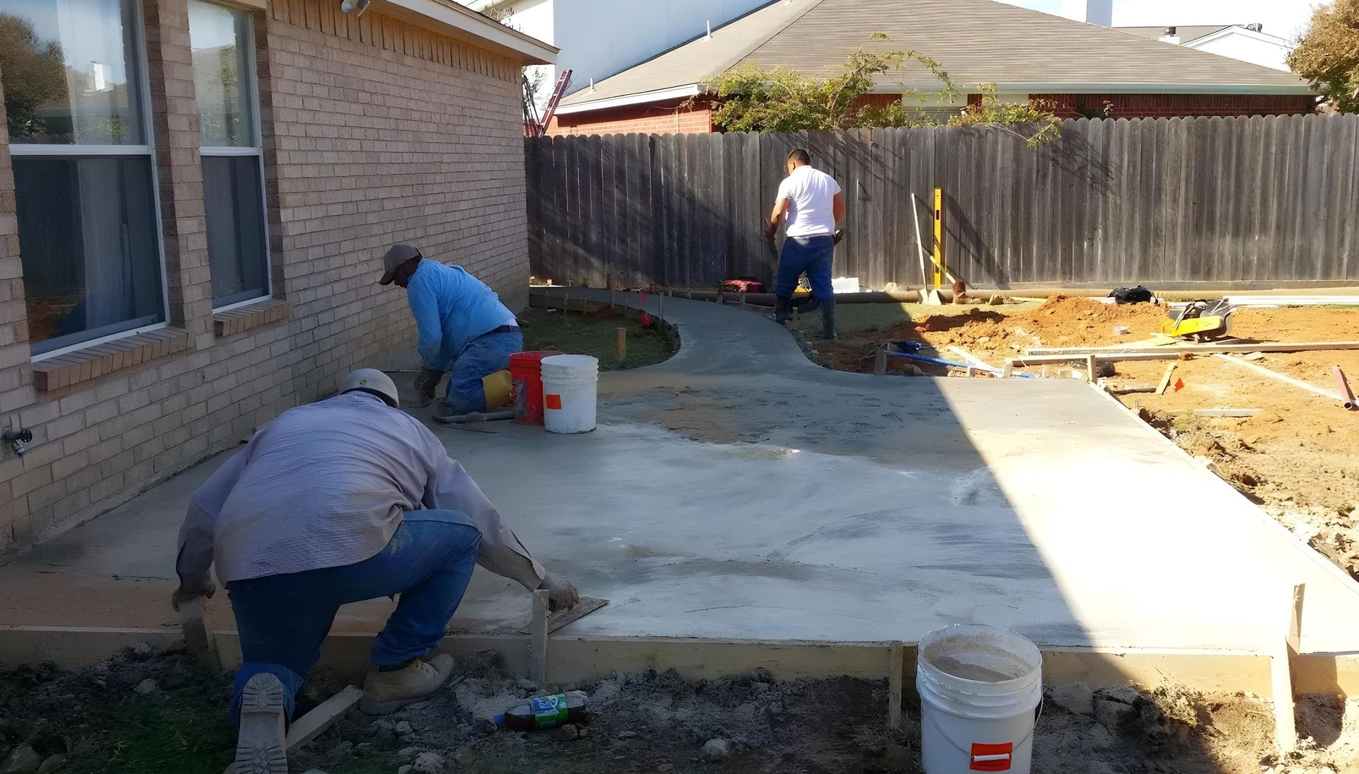A group of men are working on a concrete walkway in front of a house.