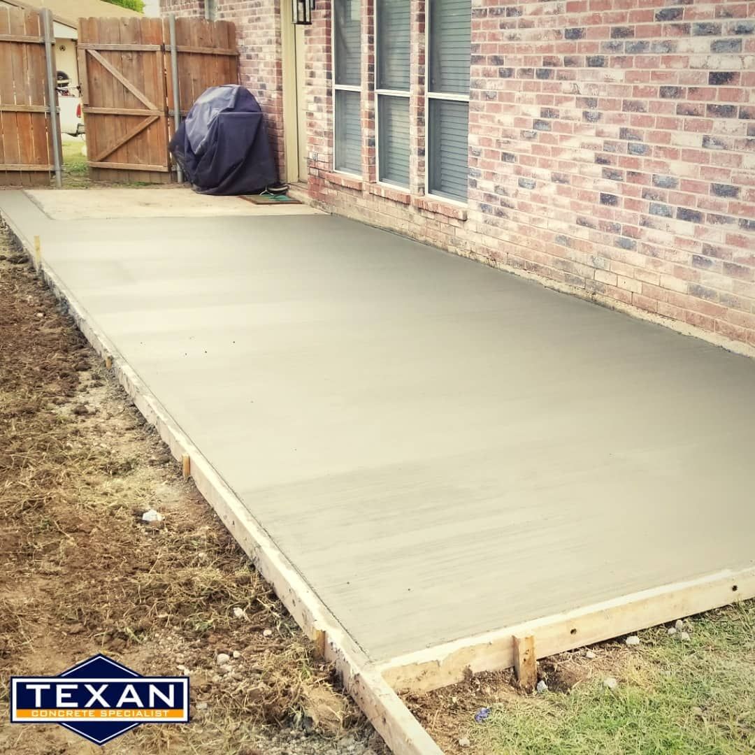 A concrete patio is being built in front of a brick house.