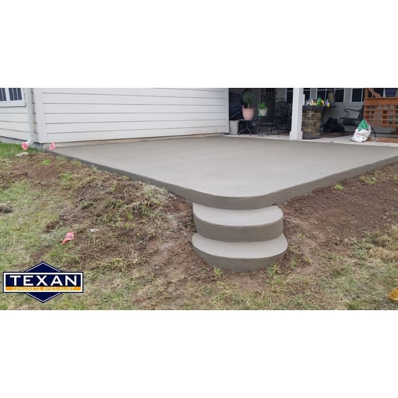 A concrete patio with steps leading up to it is being built in front of a house.