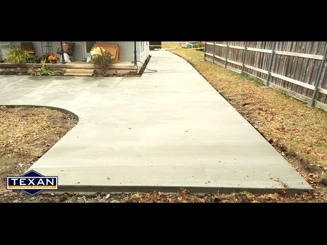 A concrete walkway leading to a house with a wooden fence.